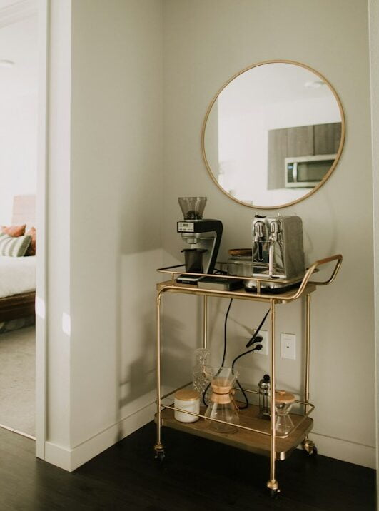 Golden bar cart in front of wall with hanging circle mirror