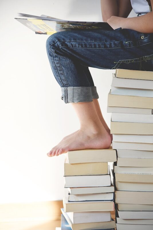 bare foot child sitting on pile of books while reading