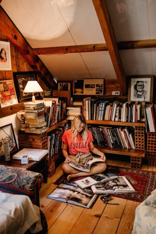 blonde girl in red shirt sitting on floor surrounded by books