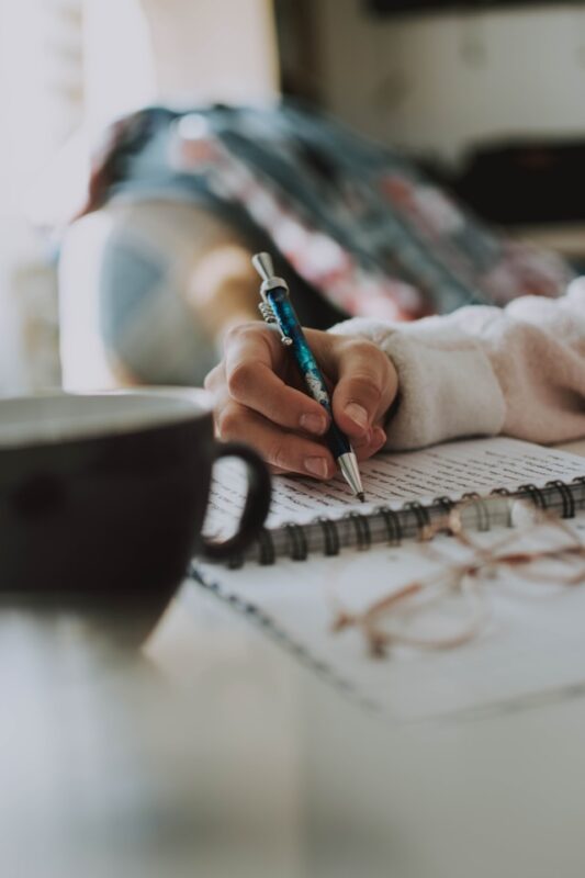 hand holding a pen and writing a plan to clean your messy house in spiral notebook