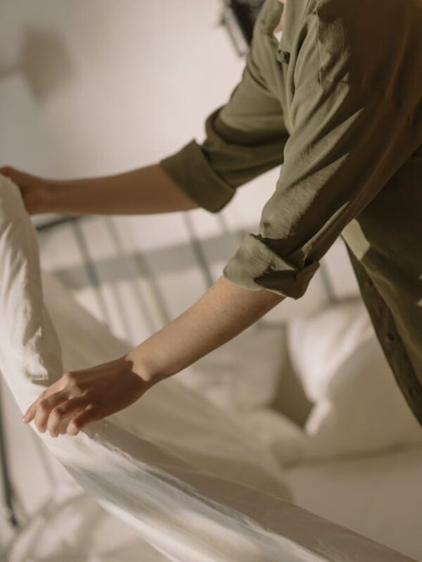 person in green shirt making a bed with white sheets