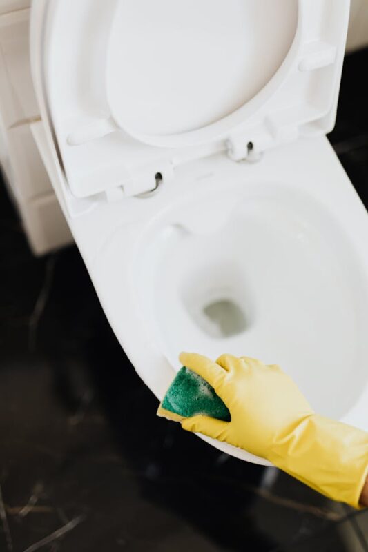 person with yellow gloves scrubbing a toilet seat