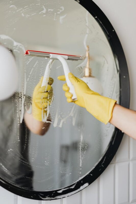 person with yellow gloves cleaning a circle mirror 