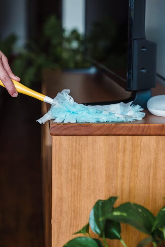 person cleaning their messy house by dusting tv stand 