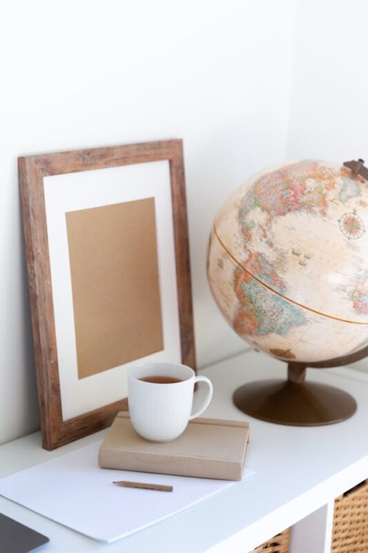 beige globe and wooden frame sitting on white shelf next to a cup of coffee