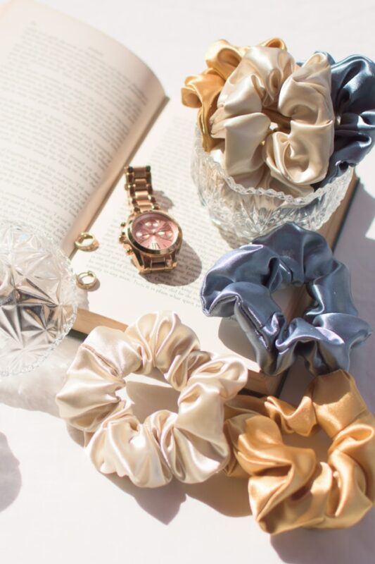 collection of multi-colored silk scrunchies and jewelry on an open book