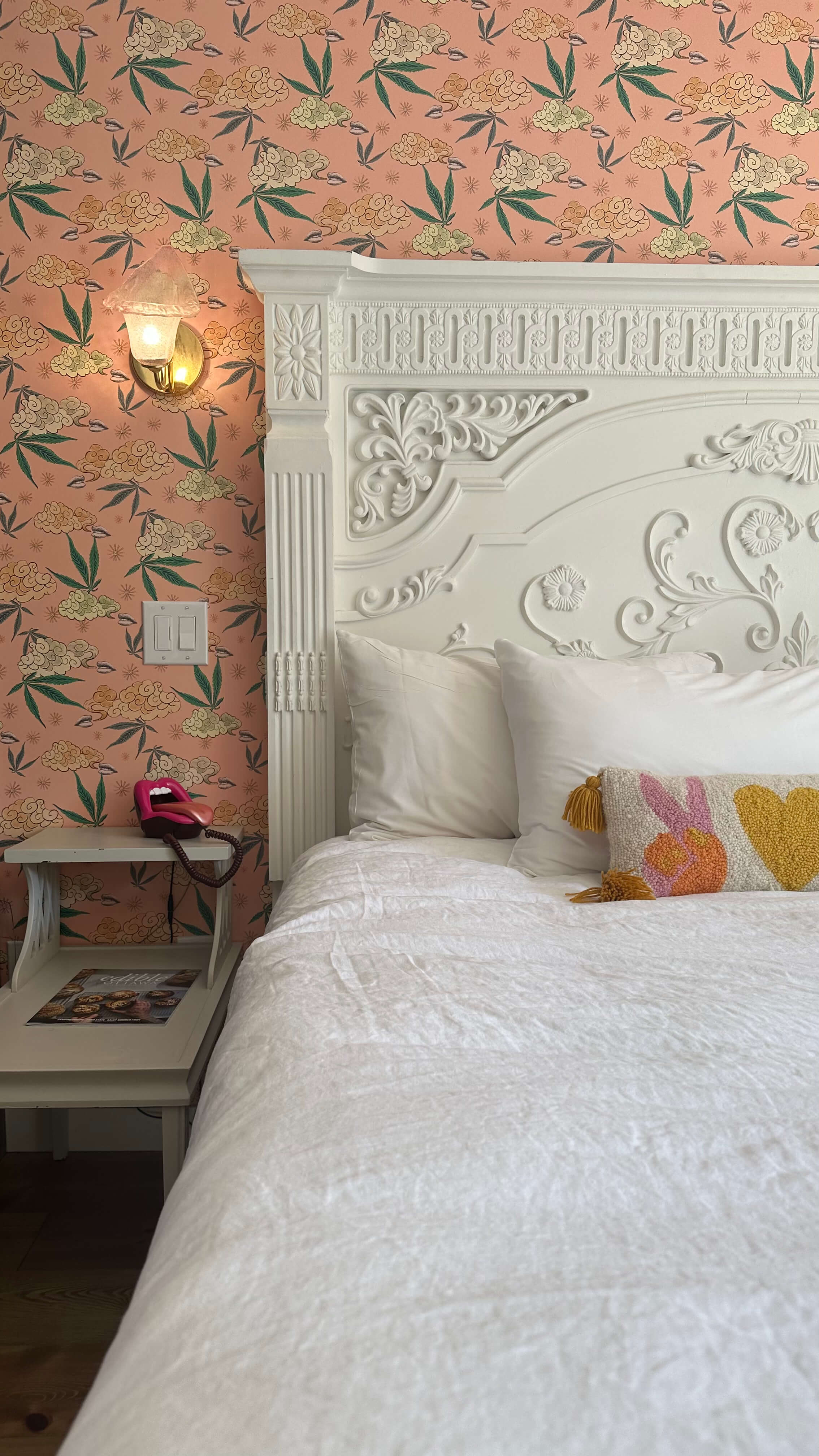 maximalist bedroom with pink and green wallpaper behind a white headboard