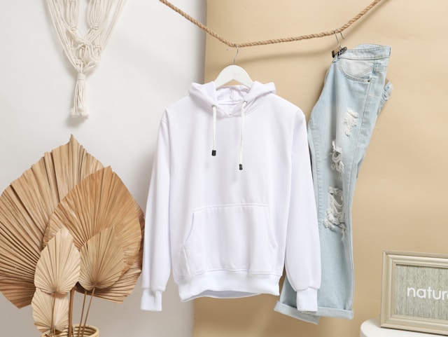 white hoodie hanging on rope hanger next to blue jeans 