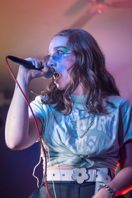 young girl in blue glasses singing into a microphone