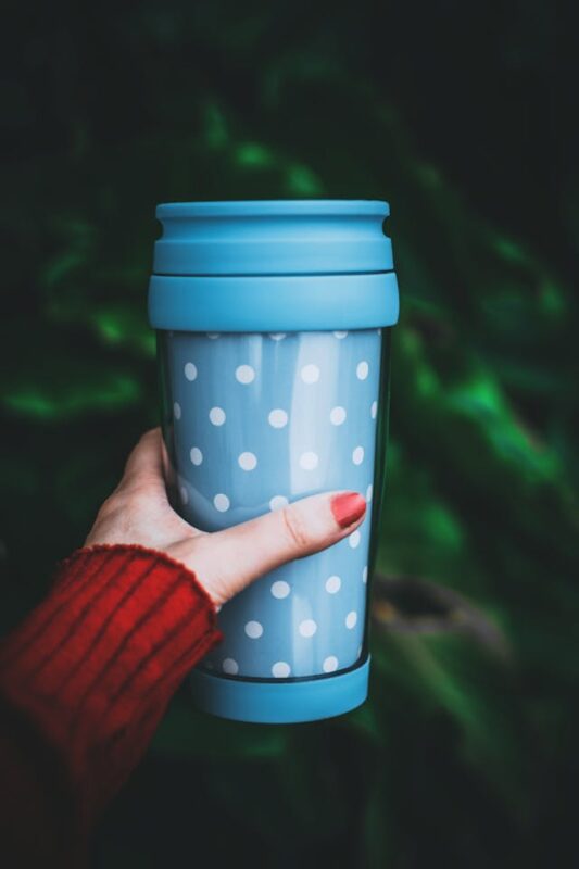 girl in red sweater holding a blue travel coffee mug with white polka dats