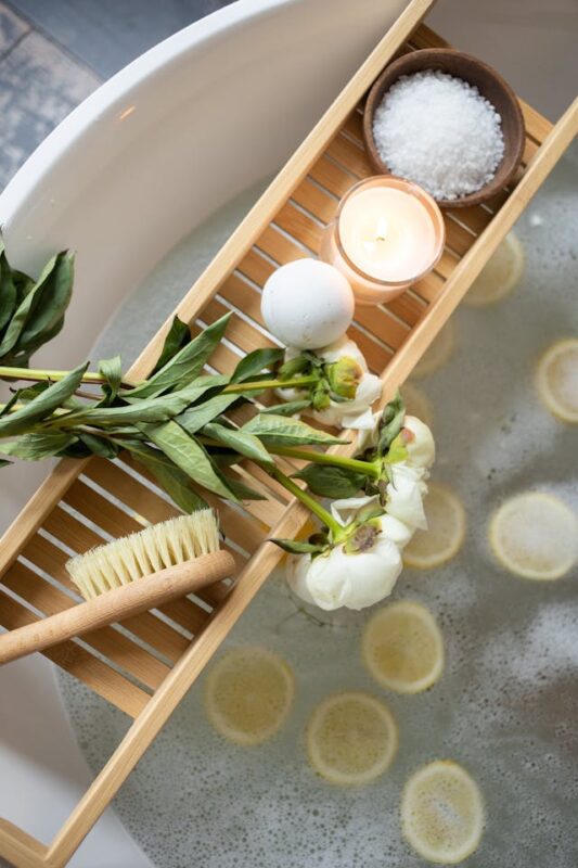 wooden bath tray holding a white bath bomb, bath salt, flowers, and a candle. 