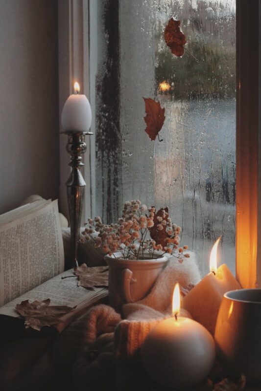 cozy reading nook by rainy window with lit candles and an open book