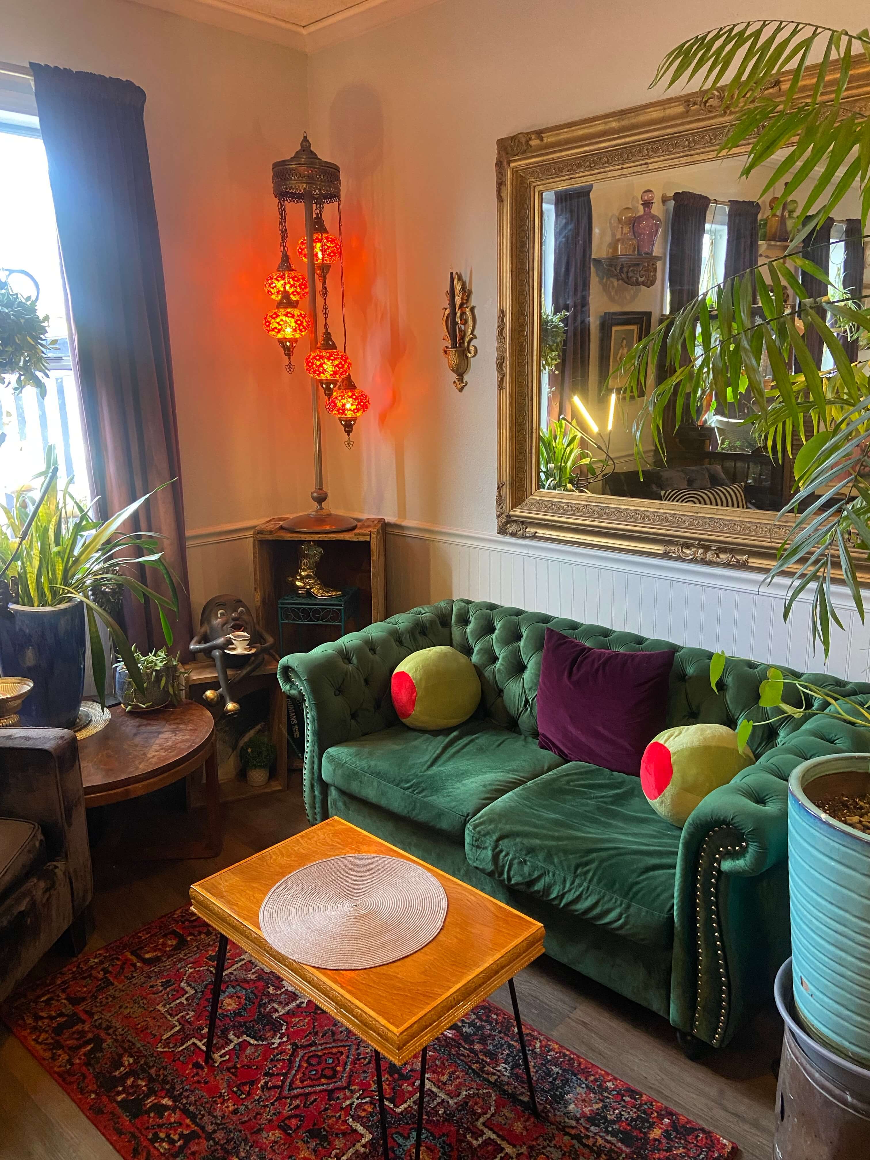 large gold framed mirror with dark green velvet couch in maximalist living room