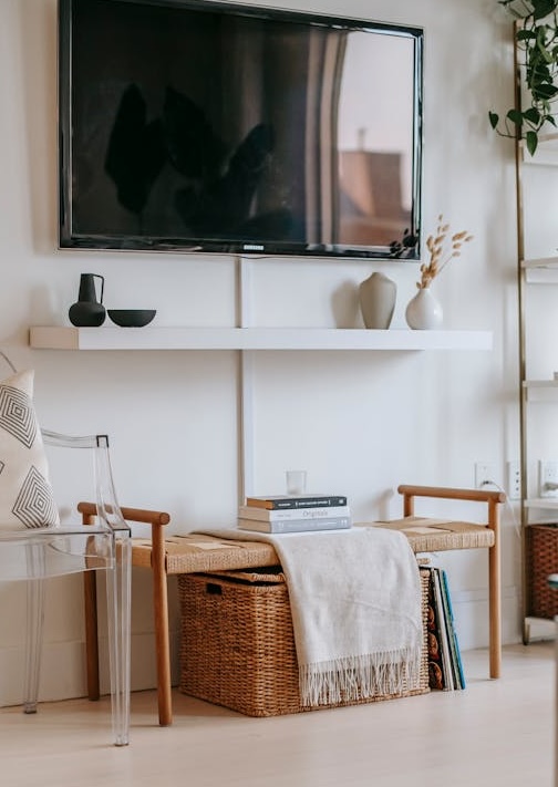 blank tv hanging on wall above floating mantel with a wicker bench beneath it