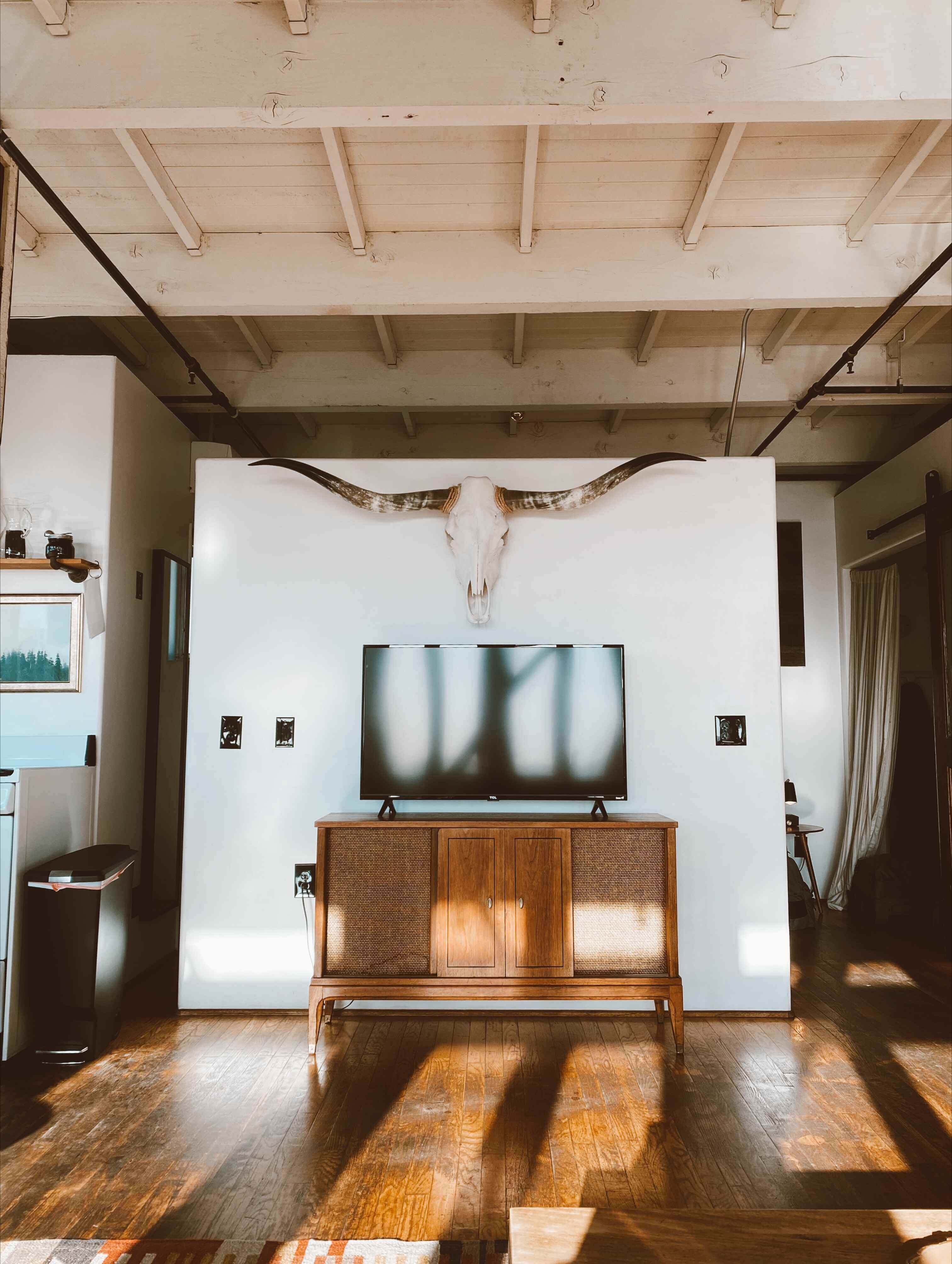 blank tv sitting on wooden console table with large steer horns hanging above it