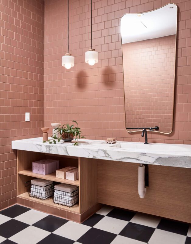 uniquely-shaped bathroom mirror with pink tile walls and white marble countertops