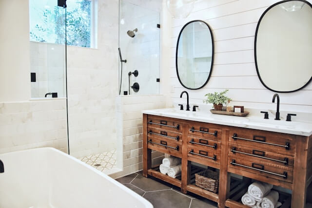 black-framed oval bathroom mirror with rustic cabinets and white tile